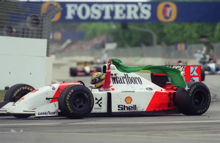 Ayrton Senna em sua última vitória na Formula 1. Ele está na mclaren branca e vermelha, segurando a bandeira do brasil. Imagem destacada do post do site F1 Hoje.